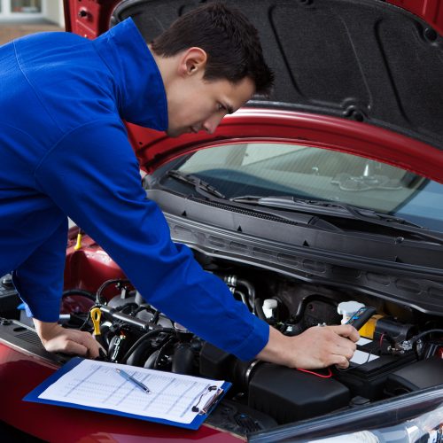 Side view of young mechanic in uniform repairing car